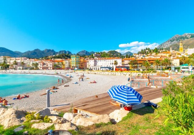 Tourists and locals enjoy a sunny day on the French Riviera as they relax on the sandy Plage de Fossan Mediterranean beach in Menton, France