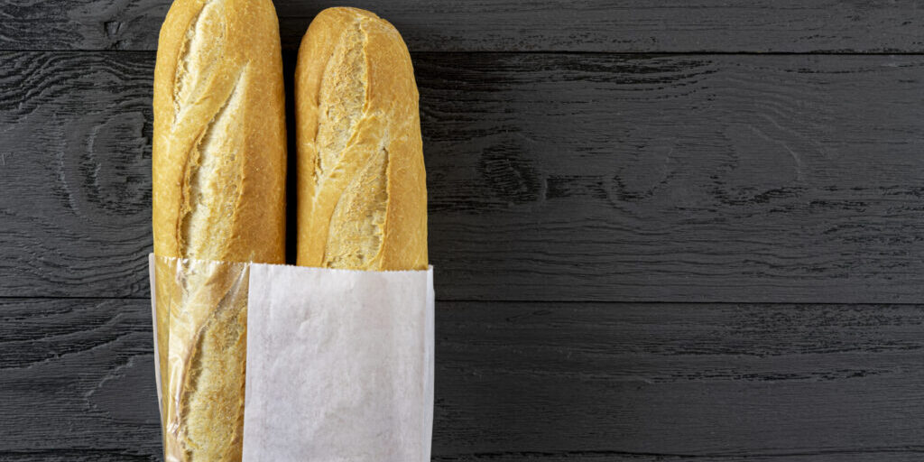 French bread mini baguette in a paper bag on a black wooden tabl