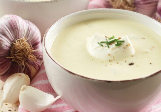 Homemade Garlic Soup surrounded by Ingredients on a Pink and Wooden Background