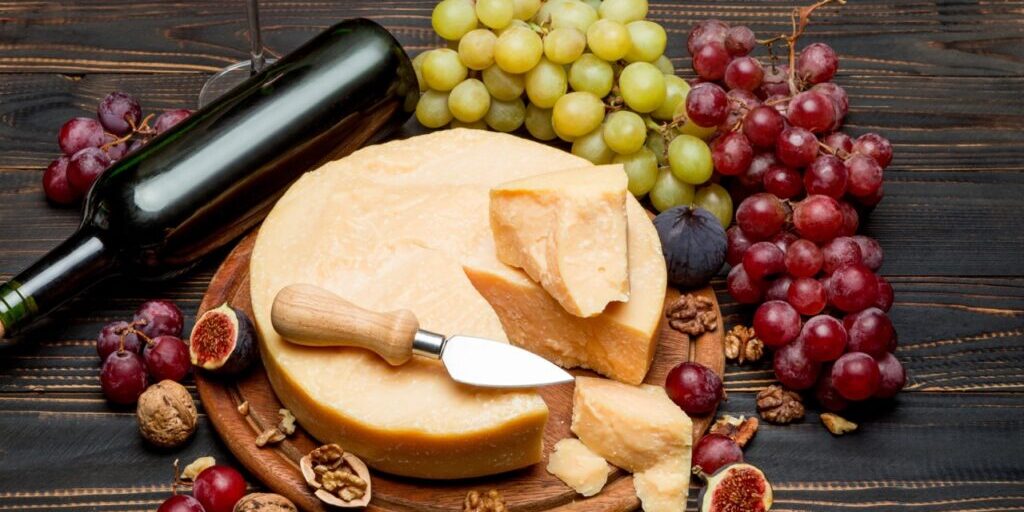 Whole round Head parmesan cheese, wine and grapeson wooden cutting board